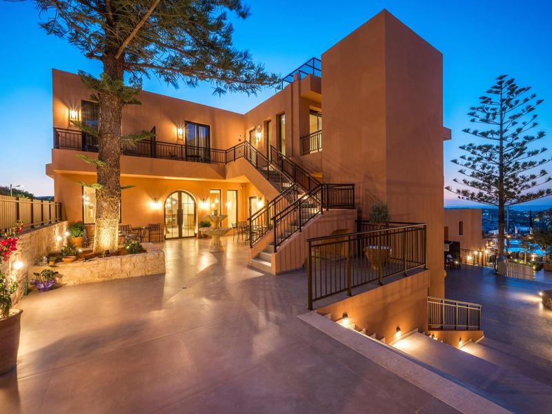 Modernes Haus mit Terrasse und Treppe, warm beleuchtet, umgeben von Bäumen und Abendhimmel.