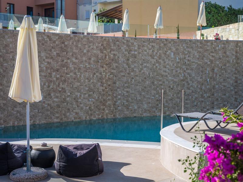 Pool mit türkisfarbenem Wasser, Liegestühle, Sonnenschirme und lila Blüten im Vordergrund.