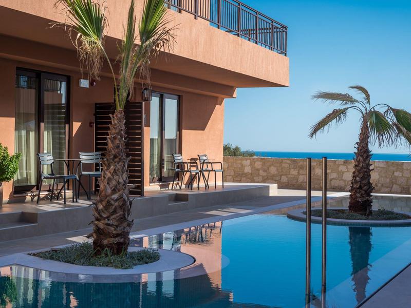 Moderner Pool mit zwei Palmen und Terrasse an einem orangefarbenen Gebäude bei klarem Himmel.