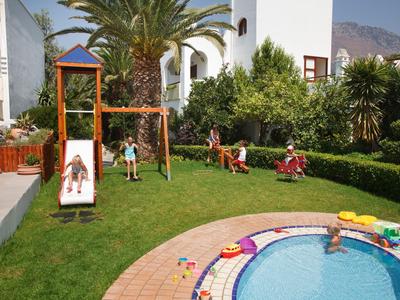 Kindergarten mit Spielplatz, Rutsche, Schaukel, Kindern und kleinem Pool in einem Garten.