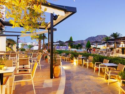 Freiluftrestaurant mit Holzmöbeln, blühenden Pflanzen und Bergen im Hintergrund bei Abendlicht.