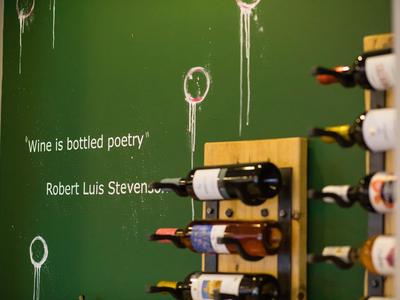 Grüne Wand mit Weinflaschenhalterungen und weißer Schrift mit Robert Luis Stevenson Zitat.