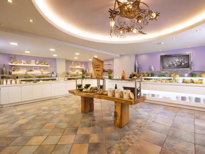 Área de buffet de hotel bien iluminada con mostradores de comida y mesa redonda de madera.
