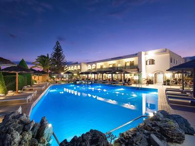 Modern hotel met verlicht buitenzwembad en ligstoelen bij schemering.