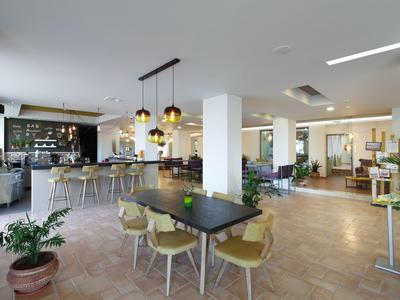 Nowoczesne lobby hotelowe z barem, stołami, krzesłami i roślinami w jasnym pomieszczeniu.