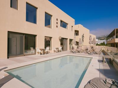 Complejo hotelero moderno con piscina rectangular y tumbonas bajo un cielo azul brillante.