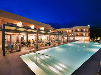 Piscina moderna de hotel con agua iluminada y área de descanso por la noche.