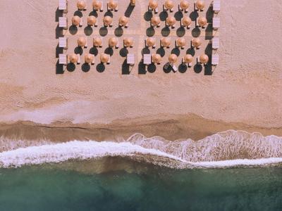 Vista de dron de una playa con tumbonas y sombrillas, costa arenosa y agua verde.