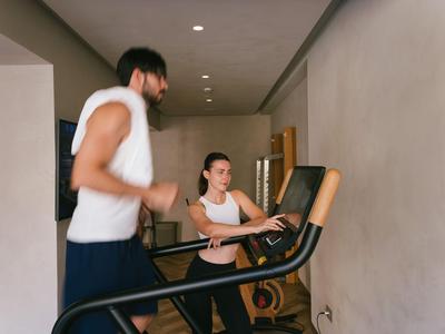 Dos personas entrenan en cintas de correr en una habitación interior luminosa con paredes blancas.