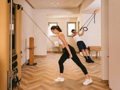 Dos personas entrenan con bandas de resistencia en un gimnasio luminoso de hotel.