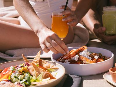 Dos personas se relajan con bebidas coloridas y platos de comida sobre una mesa.