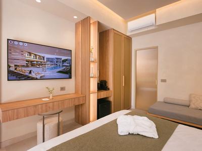 Habitación de hotel moderna con TV de pantalla plana, cama y zona de estar en tonos cálidos.