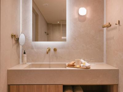 Baño moderno de hotel con espejo iluminado y toallas debajo del mostrador.