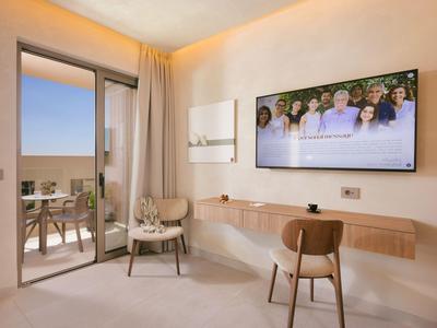 Habitación de hotel moderna con televisor, escritorio, sillas y balcón con vista al mar.