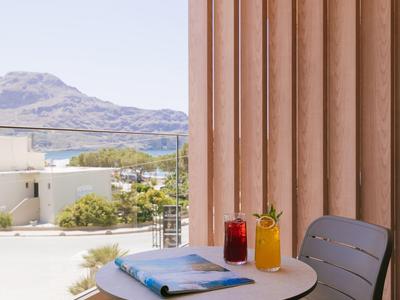 Balcón con silla moderna, mesa redonda, bebidas y vista a montañas y edificios.