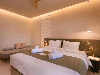 Habitación de hotel moderna con cama grande, sofá gris y luz cálida.