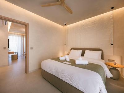 Habitación de hotel moderna con cama doble, sábanas blancas, luz cálida y acceso a una habitación contigua.