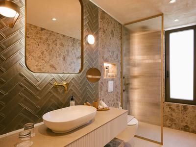 Baño luminoso con lavabo ovalado, grifería dorada y azulejos de mármol.