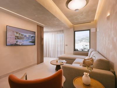 Habitación de hotel moderna con sofá, sillón, ventana y televisor en la pared.