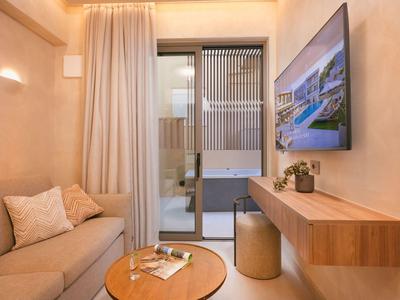 Área moderna de habitación de hotel con sofá, mesa de madera, TV y puerta transparente al balcón.
