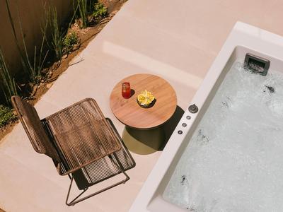 Silla moderna y mesa de madera junto a un jacuzzi con bebidas sobre la mesa.