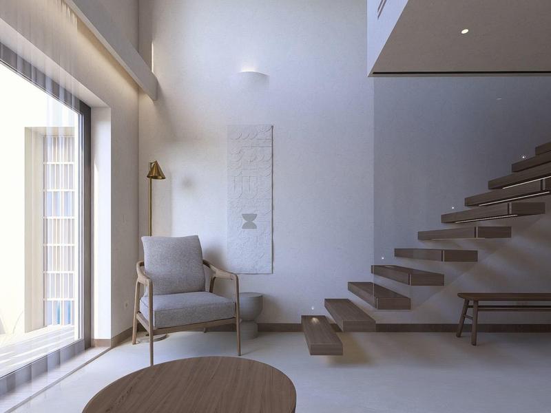 Lichte woonkamer met grote ramen, grijze fauteuil en zwevende houten trap.