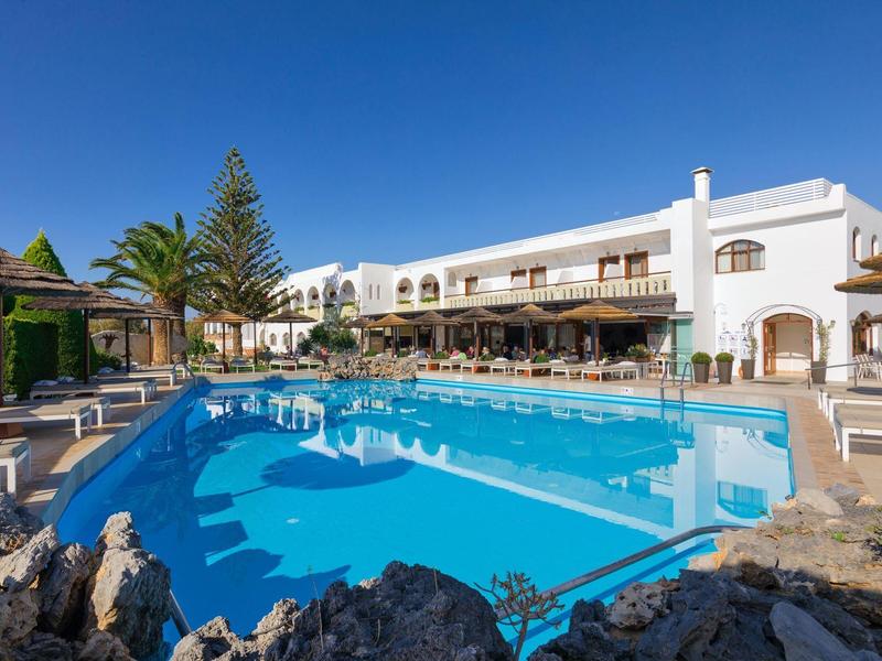 Hotel met groot buitenzwembad, omgeven door ligstoelen en een heldere blauwe lucht.