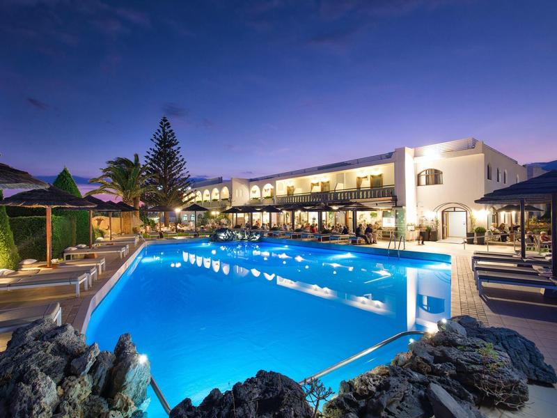 Modern hotel met verlicht buitenzwembad en ligstoelen bij schemering.