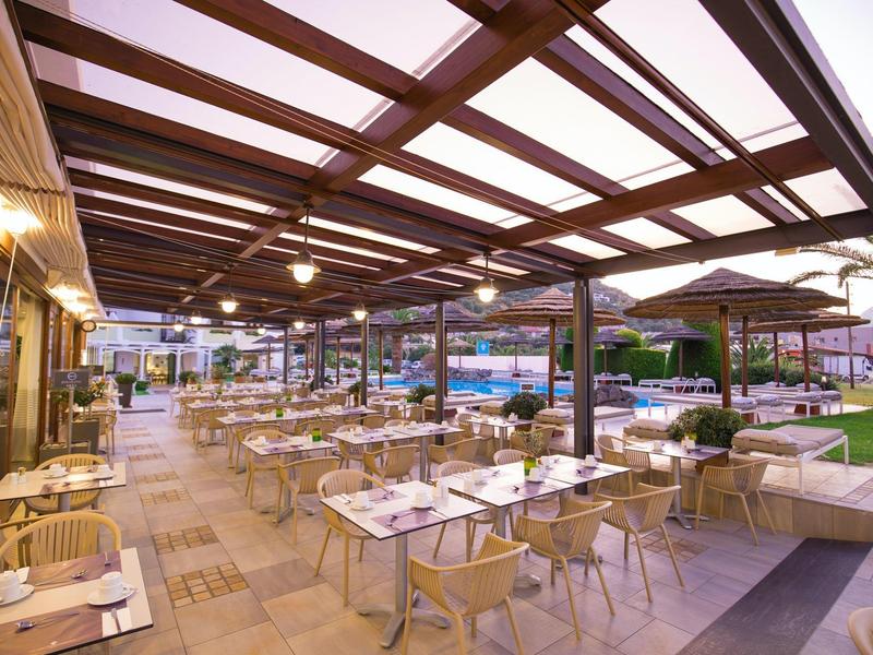 Overdekt buitenterras met tafels, stoelen en uitzicht op het zwembad.