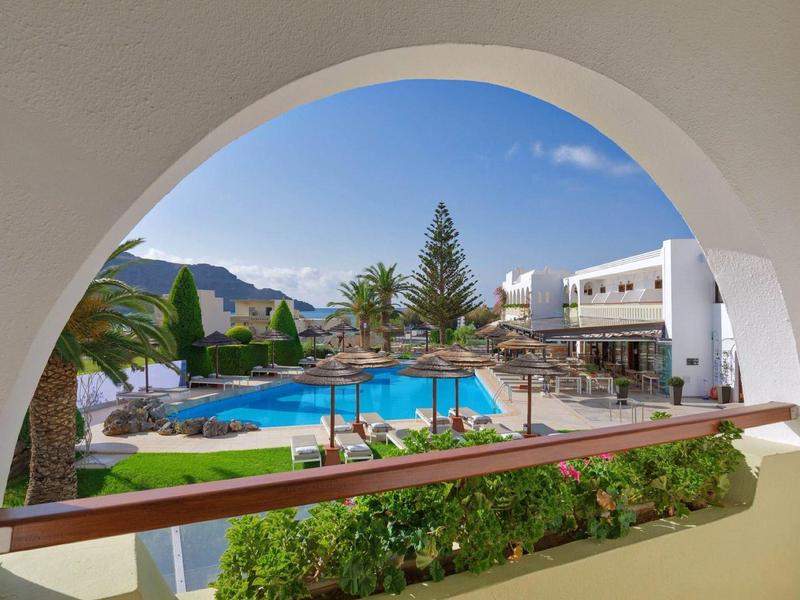 Uitzicht door een boog op een zwembad met ligstoelen en gebouwen op de achtergrond