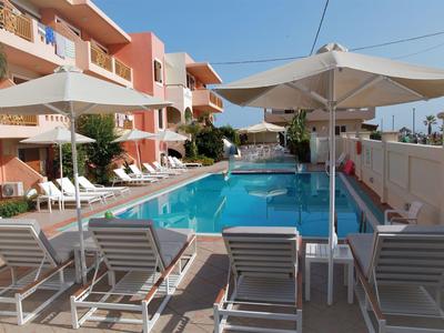 Piscina all'aperto con lettini bianchi e grandi ombrelloni davanti a un edificio alberghiero sotto un cielo sereno.