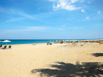 Breiter Sandstrand mit Sonnenschirmen und klarem blauem Himmel am Meer.