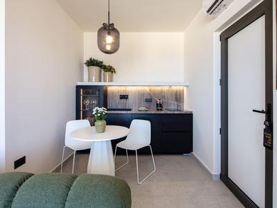 Moderner Essbereich mit runder weißen Tisch, zwei weißen Stühlen und schwarzer Küchenzeile im Hintergrund.