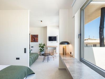 Helles, modernes Schlafzimmer mit großem Fenster, grünem Bett, TV und schlichtem Tisch mit Stühlen.