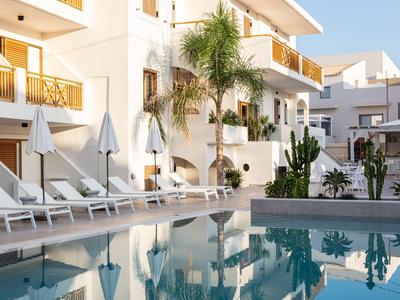 Piscina moderna dell'hotel con lettini e palme davanti a un edificio bianco alla luce del giorno.