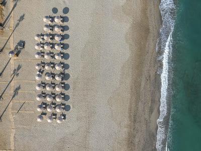 Vogelperspektive auf strand mit Reihen von Sonnenschirmen, Sand und sanften Wellen am Ufer.