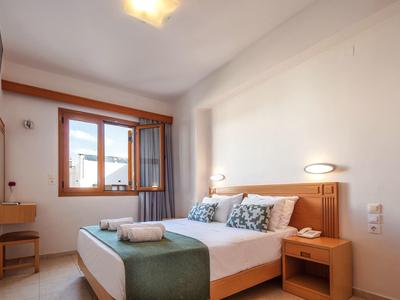 Hell eingerichtetes Schlafzimmer mit Doppelbett, Holzmöbeln, grünem Bettläufer und Fenster mit Vorhängen.