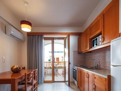 Kleine Küche mit Holzschränken, Tisch, Stühlen, Kühlschrank, Mikrowelle und Terrassentür.