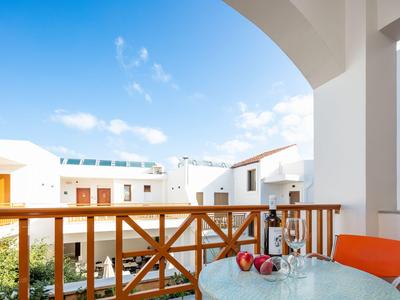 Balcone con ringhiera in legno, tavolo di vetro e vista su edifici bianchi e cielo blu.