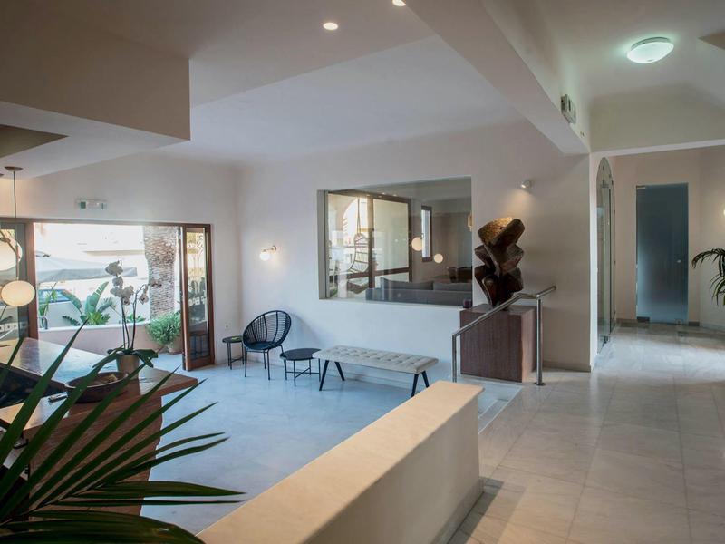 Heller, moderner Innenraum mit weißen Wänden, Sitzgelegenheiten und großen Fenstern bei Tageslicht.