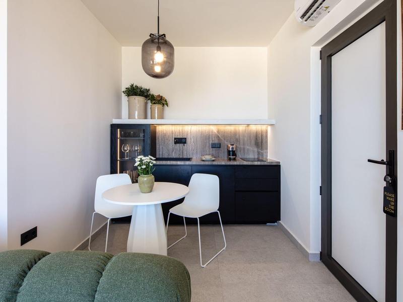 Moderner Essbereich mit runder weißen Tisch, zwei weißen Stühlen und schwarzer Küchenzeile im Hintergrund.