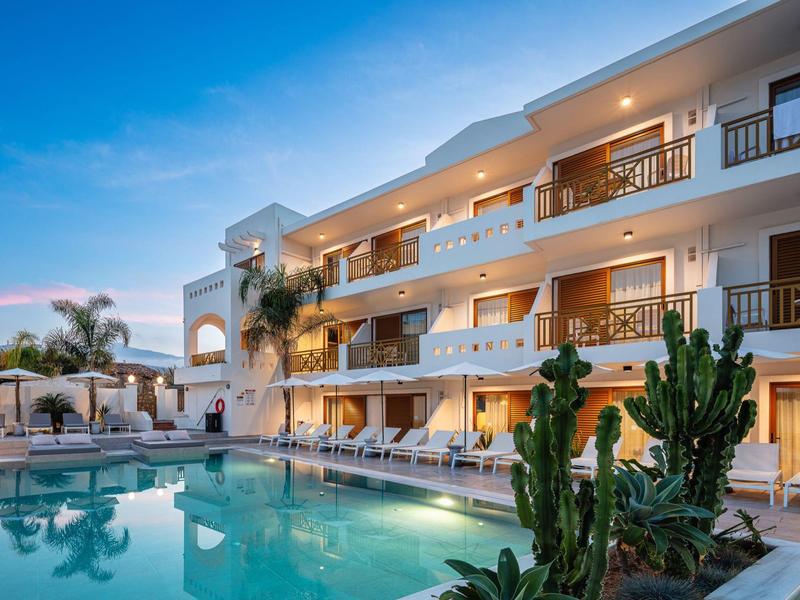 Moderner Hotelkomplex mit beleuchtetem Pool, mehreren Balkonen und Pflanzen bei Dämmerung.