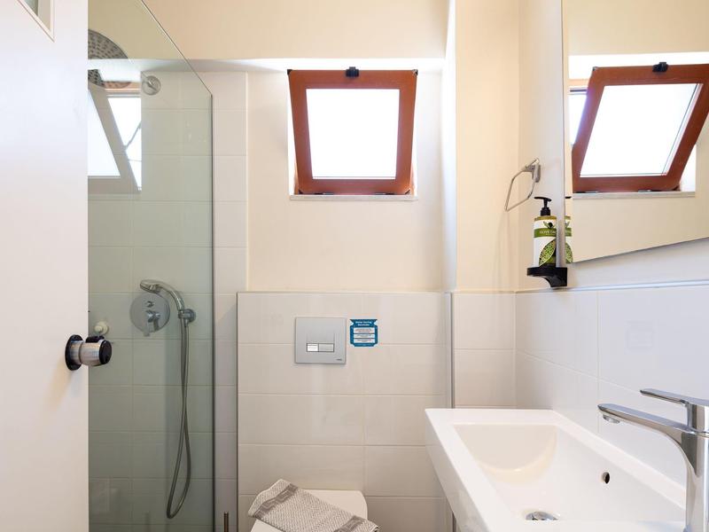 Helles kleines Bad mit Glasdusche, weißem Waschbecken und zwei kleinen Dachfenstern.