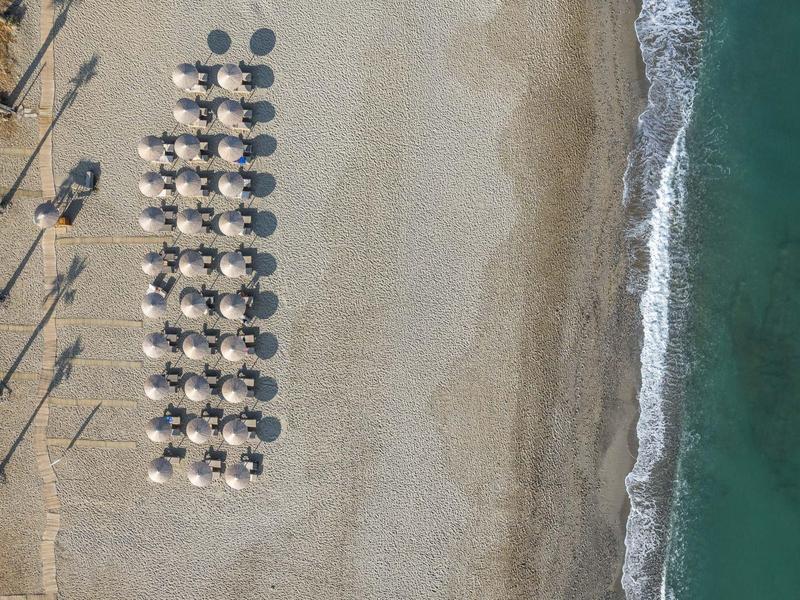 Vogelperspektive auf strand mit Reihen von Sonnenschirmen, Sand und sanften Wellen am Ufer.