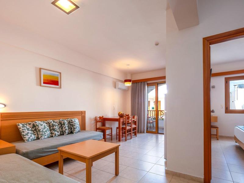 Heller Wohnraum mit Sofa, Tisch, Sesseln, Esstisch, Balkon und Blick in angrenzendes Schlafzimmer.