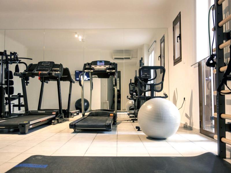Heller Fitnessraum mit Laufbändern, Gymnastikball, Trainingsgeräten und großen Spiegeln an der Wand.