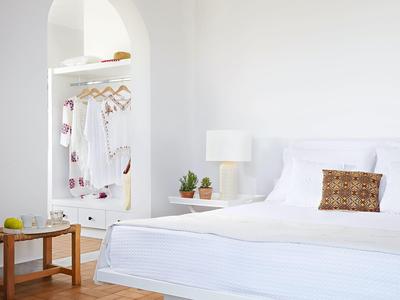 Lichte, moderne slaapkamer met wit bed, houten stoel en open kast.