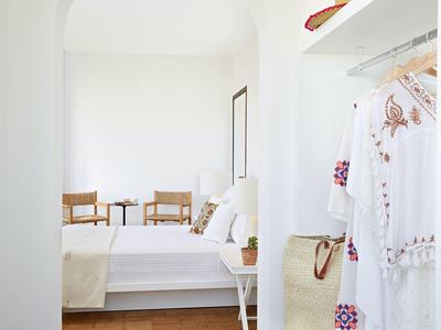 Lichte, eenvoudige hotelkamer met wit beddengoed, twee stoelen en een kleine plant.