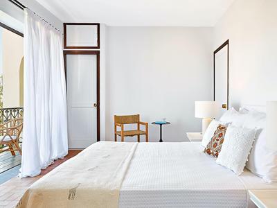 Camera luminosa arredata con letto grande, mobili in legno e balcone con tenda bianca.