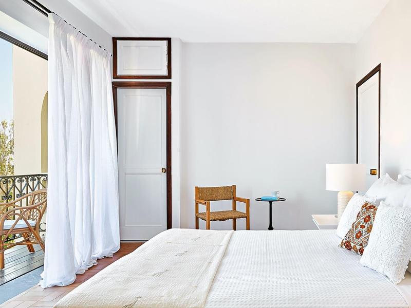 Lichte hotelkamer met tweepersoonsbed, houten meubels en balkon met uitzicht buiten.